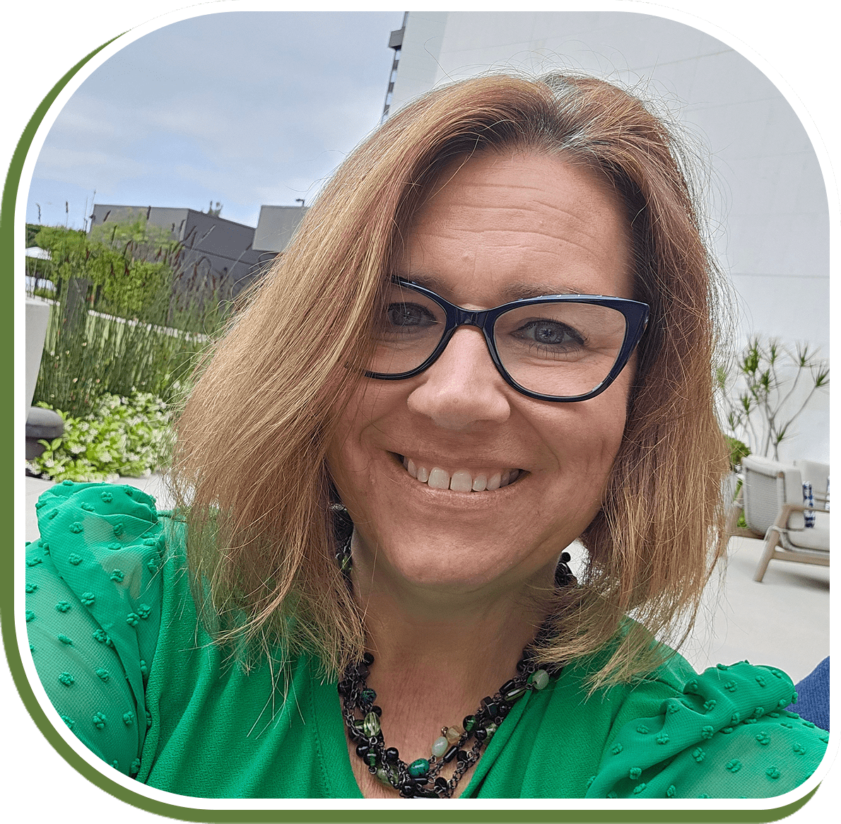 Smiling woman with glasses outdoors in a green top.